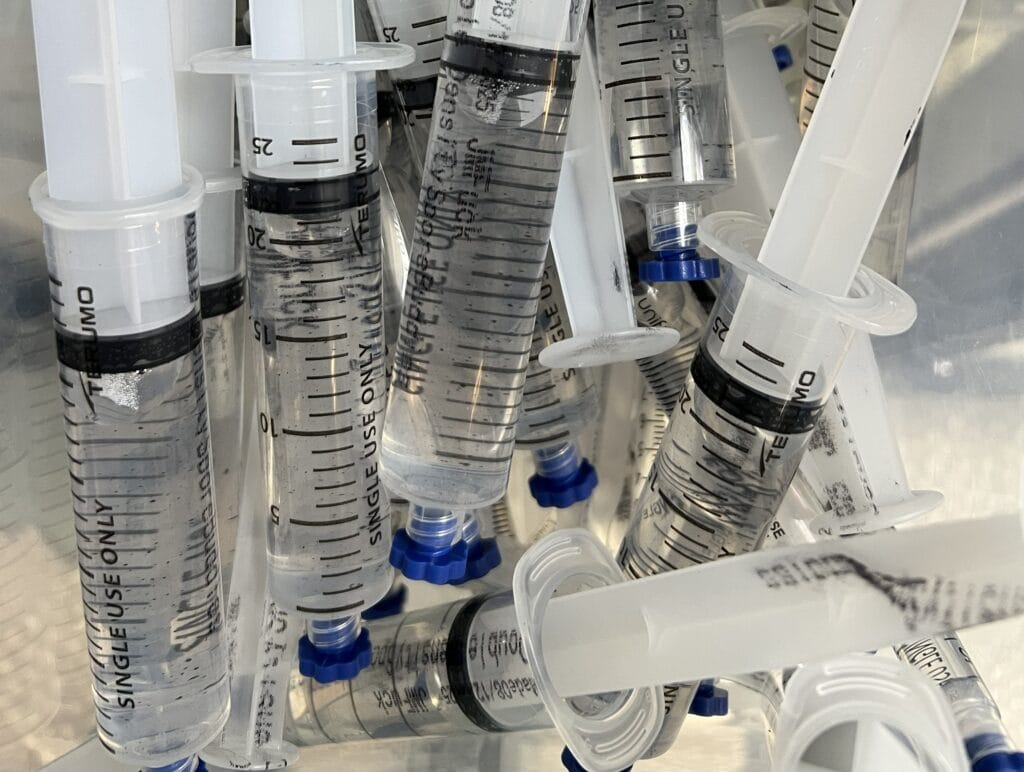 Clear psilocybe spore syringes stored in a refrigerated container at SporeBuddies, showing sterile 10ml microscopy syringes with visible spore solution.