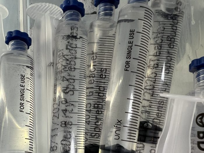 Close-up of labelled psilocybe spore syringes stored upright in a lab fridge for microscopy research.